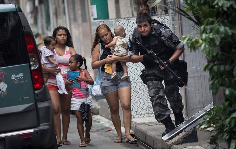 Upon hearing gun shots, a military police officer runs for cover, past residents, during an operation in the Mare slum complex, ahead of its `pacification,` in Rio de Janeiro, Brazil.