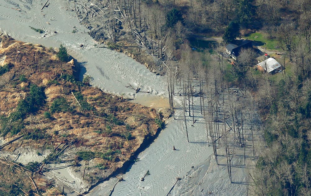 An intact house is shown at right near where water from the Stillaguamish River is flowing around the edge of the massive mudslide that killed at least eight people Saturday and left dozens missing, as shown in this aerial photo, near Arlington, Wash.