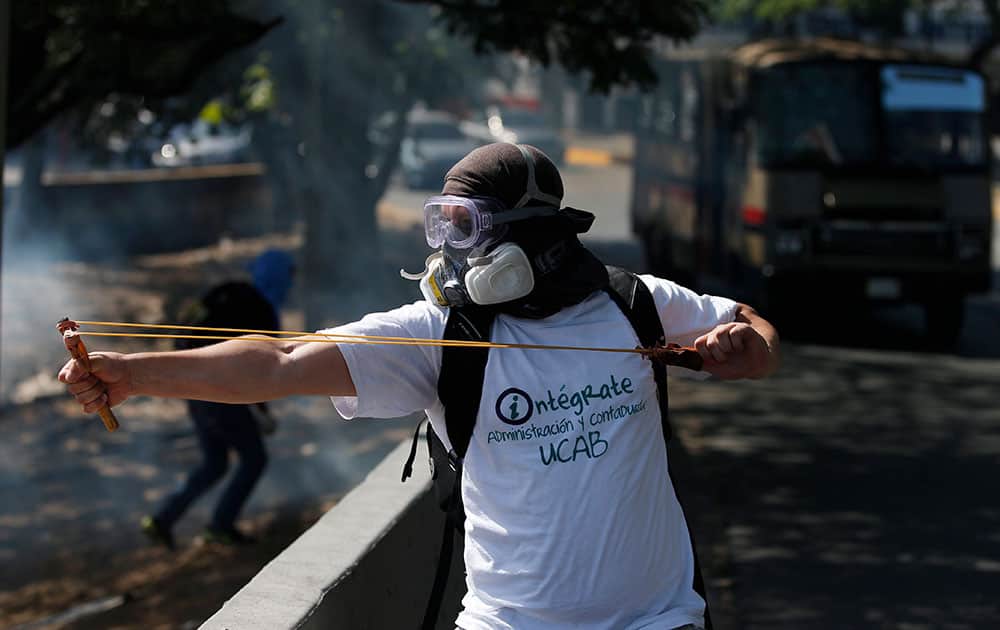 A masked anti-government protester uses a slingshot to shoot marbles at Bolivarian National guards during clashes in Caracas, Venezuela.