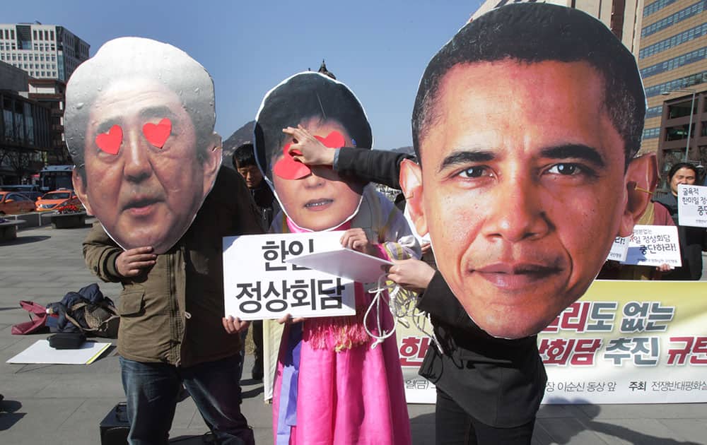 A protester wearing a mask of US President Barack Obama, puts heart-shaped stickers on masks of South Korean President Park Geun-hye, and Japanese Prime Minister Shinzo Abe, left, during a rally against their summit meeting in The Hague next week, in Seoul, South Korea.
