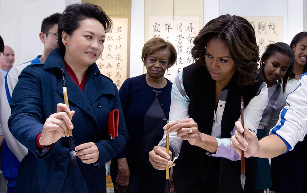 Peng Liyuan, wife of Chinese President Xi Jinping, shows US first lady Michelle Obama, center, how to hold a writing brush as they visit a Chinese traditional calligraphy class at the Beijing Normal School, a school that prepares students to go abroad in Beijing, China.