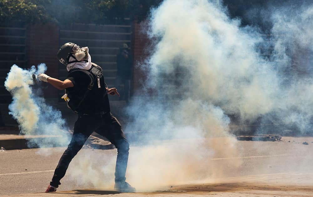A masked protester returns a tear gas canister fired by Bolivarian National Police, in Caracas, Venezuela.