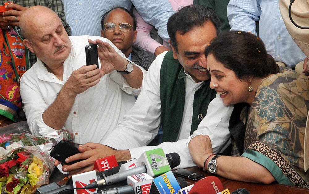 BJP Lok Sabha candidate actress Kirron Kher listens to party leader Sanjay Tandon as her husband actor Anupam Kher looks on at a press conference at the party office in Chandigarh.