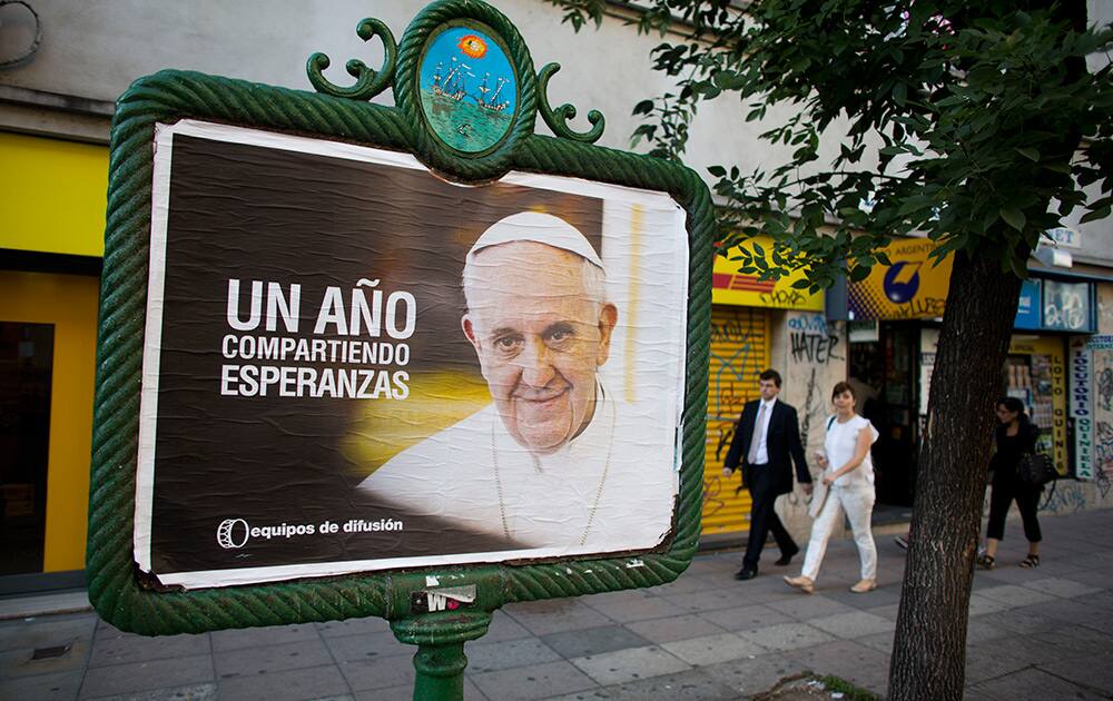 People walk by a poster of Pope Francis with a phrase that reads in Spanish `One year sharing hopes` on the day of his first election anniversary, in Buenos Aires, Argentina.