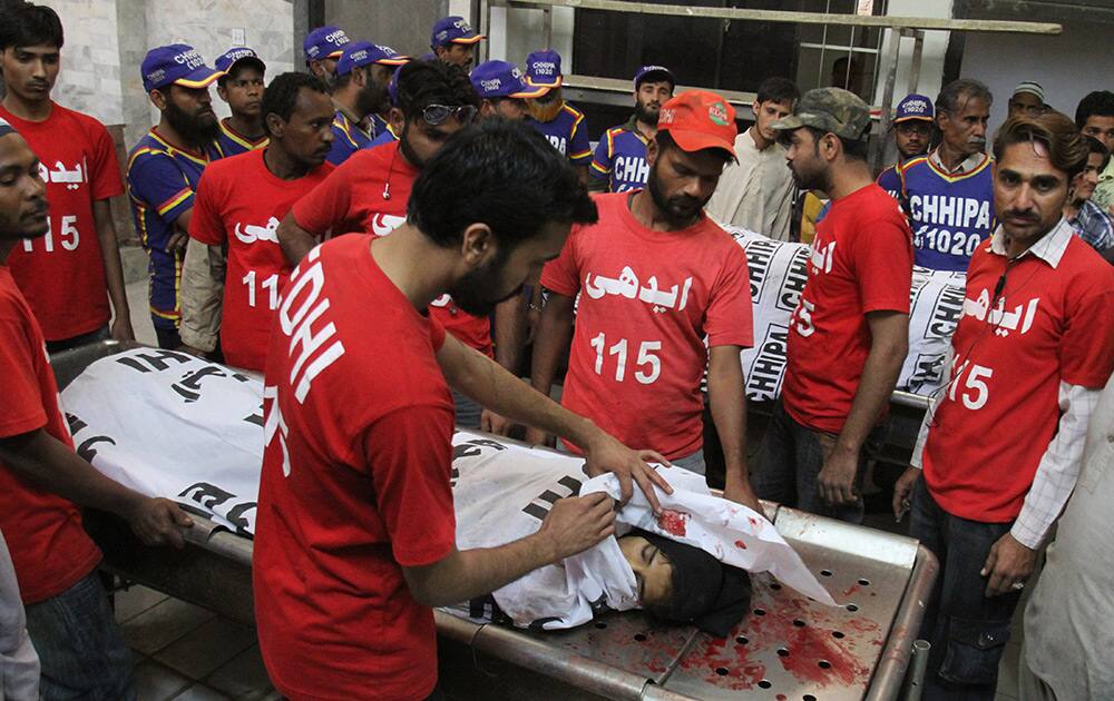 Pakistani volunteers look at a body of a woman killed in Karachi. Police in Pakistan said gang members angered over the killing of one of their leaders have opened fire on passers-by in southern Pakistan, killing a dozen people.