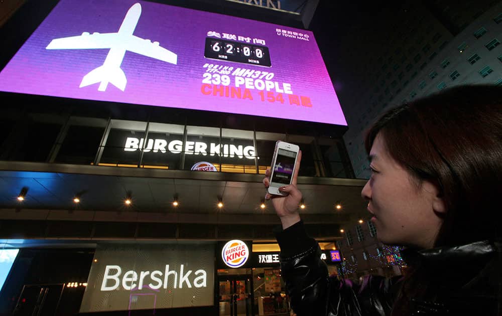 This photo shows a woman taking a photo of a screen displaying the number of hours since a Malaysia Airlines passenger jet had gone missing at a mall in Beijing, China.