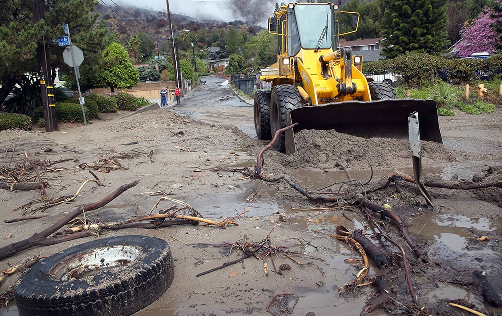 Glendora city workers clear mud and debris from the hills, in Glendora, Calif. The first wave of a powerful Pacific storm spread rain and snow early Friday through much of California, where communities endangered by a wildfire just weeks ago now faced the threat of mud and debris flows.