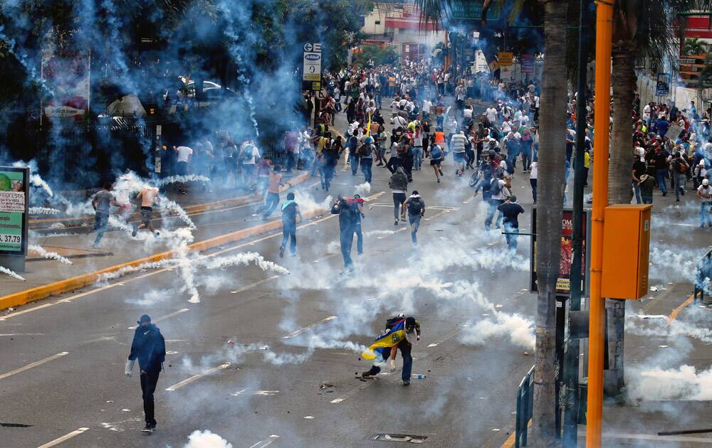 A demonstrator, bottom right, picks up a teargas canister fired by the Bolivarian National Guard as others run away as security forces disperse them from blocking a major highway in Caracas, Venezuel.