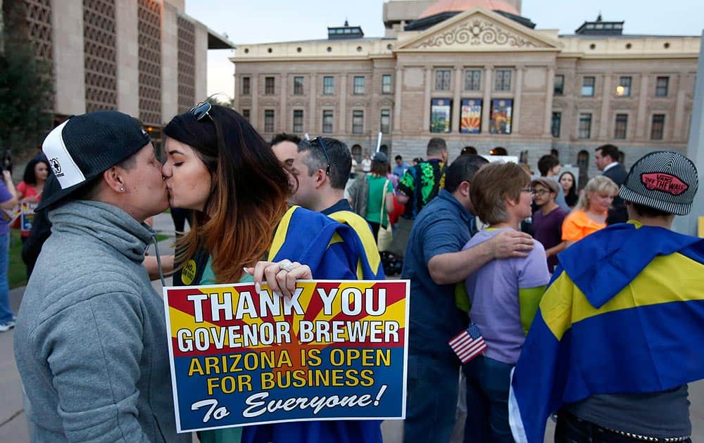 With the Arizona Capitol in the background, gay rights supporters Rachel Butas and Jo Jo Halko kiss after the two learn that Arizona Gov. Jan Brewer announces she has vetoed SB1062, a bill designed to give added protection from lawsuits to people who assert their religious beliefs in refusing service to gays, in Phoenix.