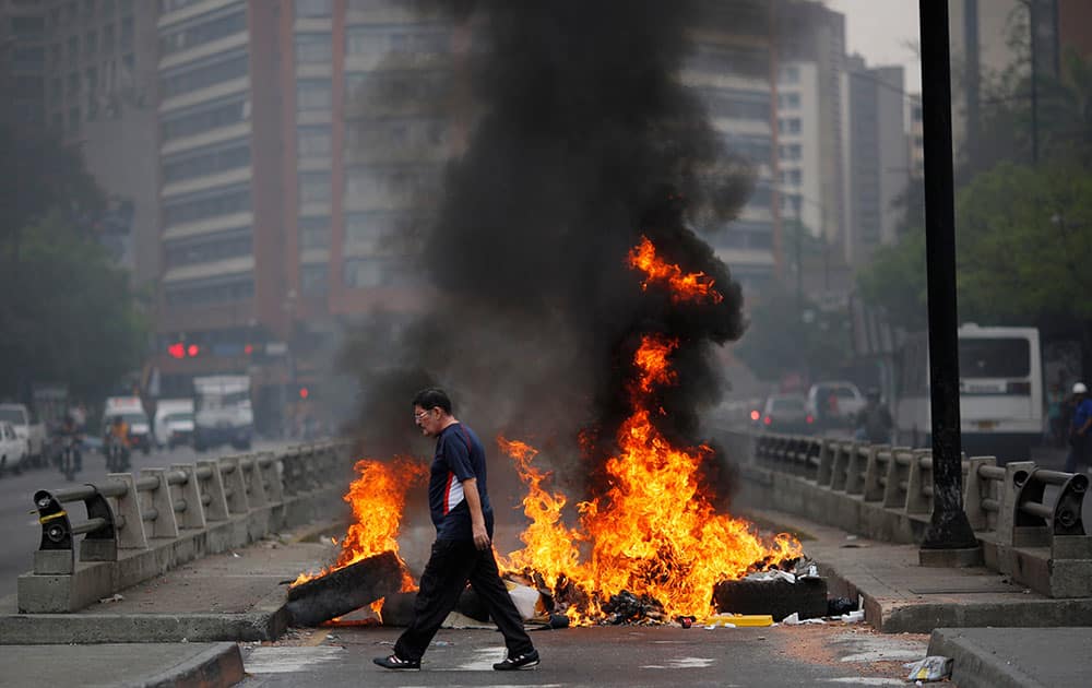 A pedestrian walks in front of a burning barricade blocking the highway in Chacao, Caracas, Venezuela.