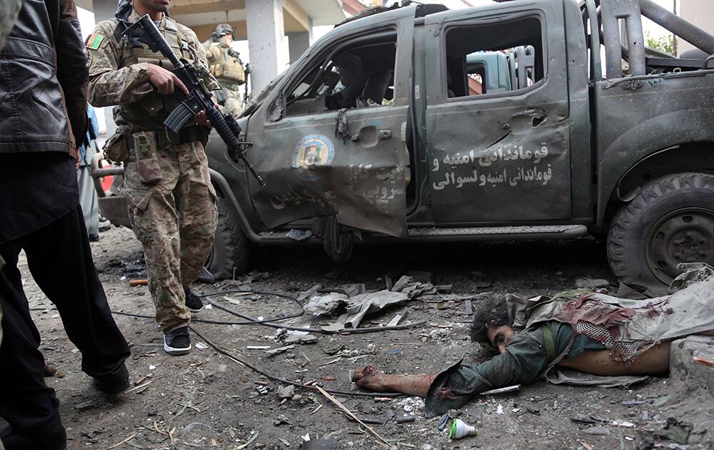 Afghan security forces stand near the body of one of suicide bombers who have attacked a police compound in Surobi district of Kabul, Afghanistan.