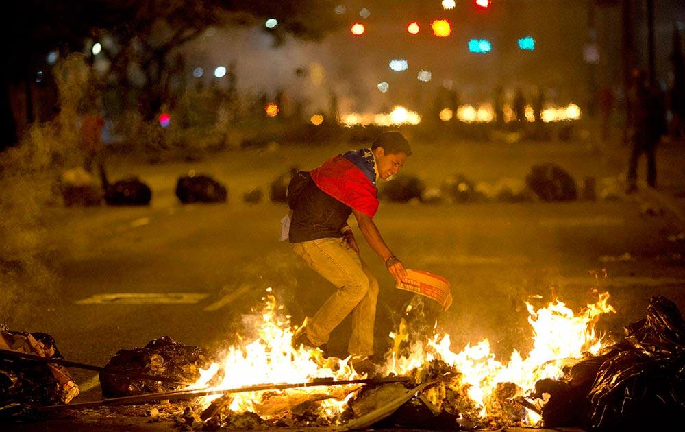 A demonstrator wearing a Venezuelan flag adds to a burning barricade in the Altamira neighborhood of Caracas, Venezuela.