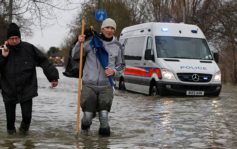 Local residents carry belongings as they walk in the flooded part of the town of Staines-upon-Thames, England, while a police van patrols the area.