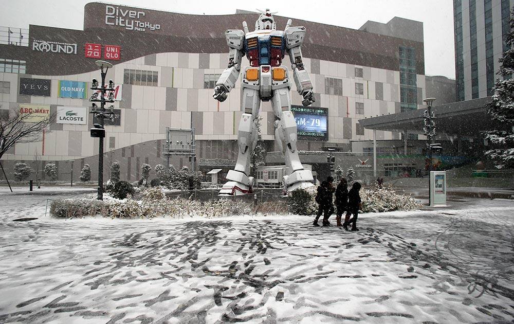 Visitors walk in the snow, in front of a full-size model of Japan`s popular robot animation character Gundam at Daiba in Tokyo.