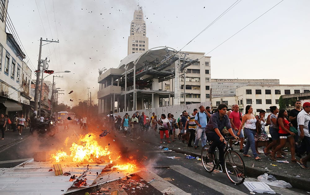 Commuters walk past a burning barricade set by demonstrators protesting a hike in bus fares, outside a train station in Rio de Janeiro.