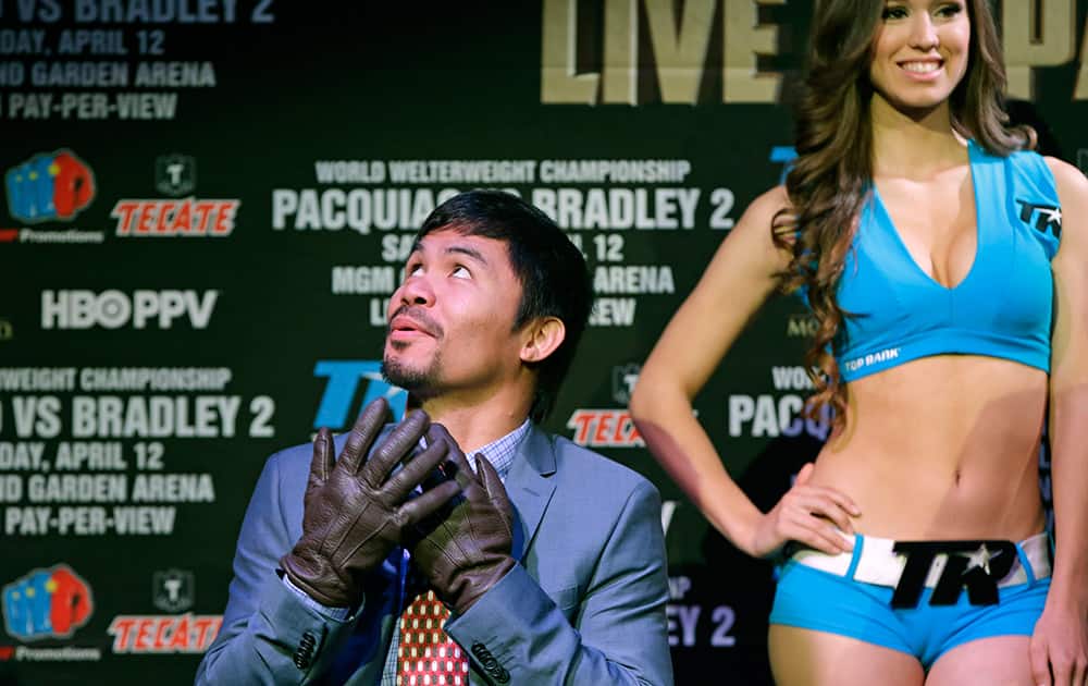 Boxer Manny Pacquiao, of the Phillipines, glances up at an air conditioning duct as he dons a pair of leather gloves while waiting to speak during a press conference in New York.