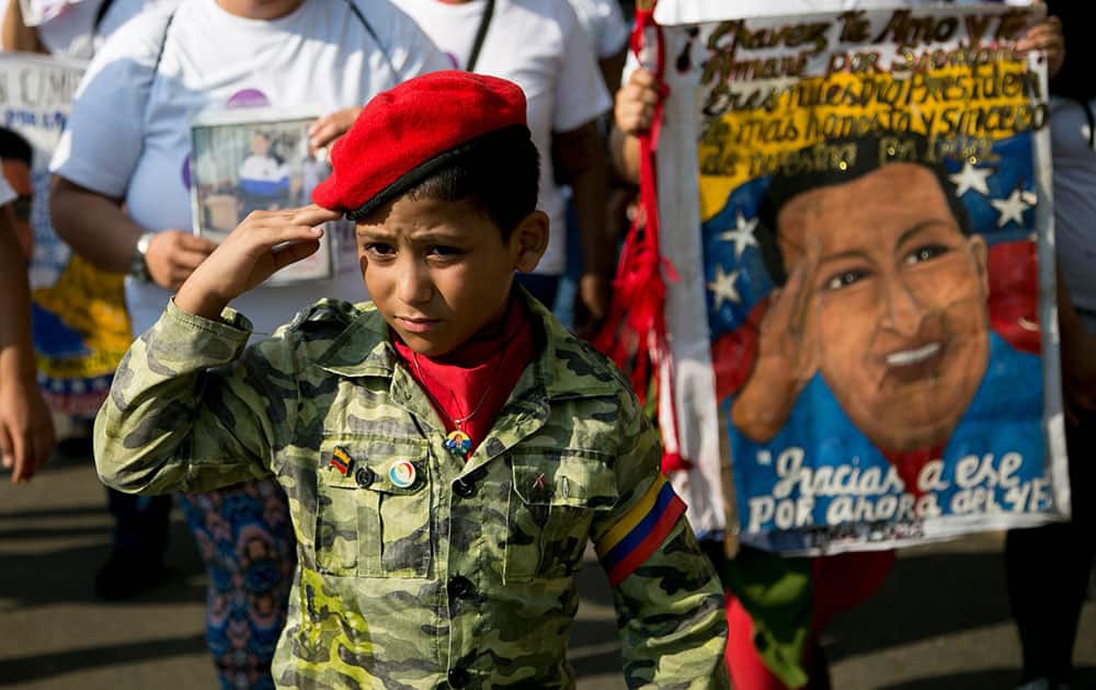 A boy dressed in a military-like uniform and a red beret salutes during an event commemorating the anniversary of a failed coup attempt led by the late President Hugo Chavez, in Caracas, Venezuela.