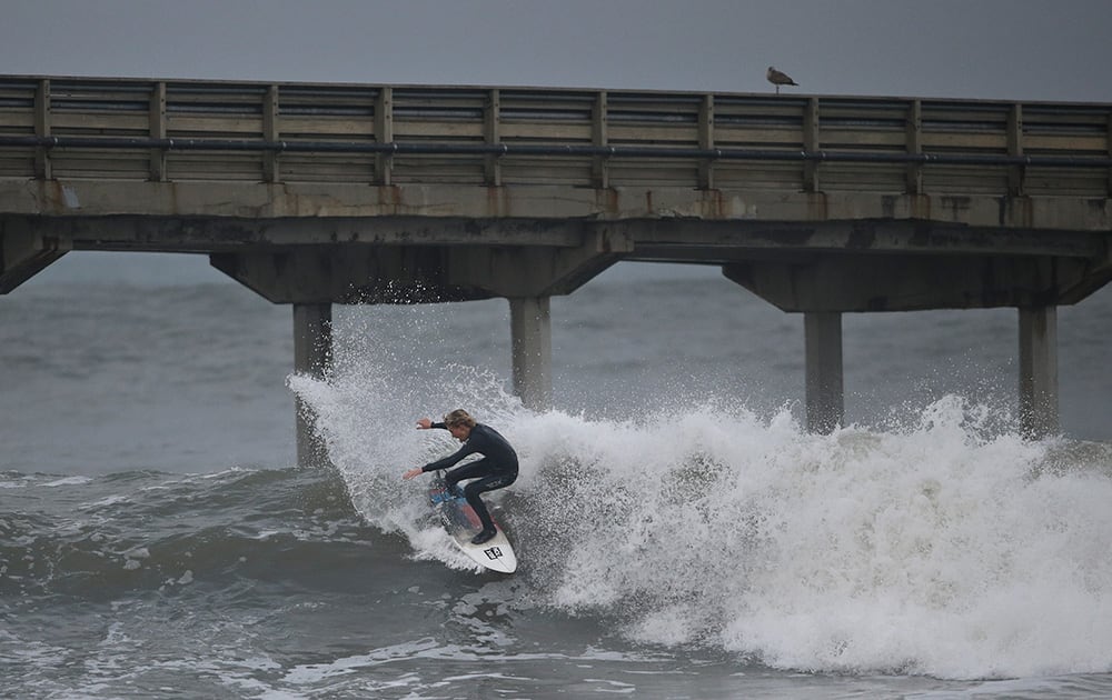 A surfer rides unusually high surf under the Ocean Beach Pier, in San Diego. For the first time in months the weather forecast in Southern California predicts rain and a winter storm.