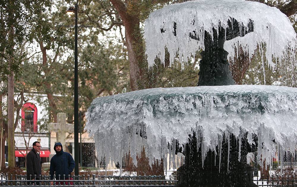 Cody Carpp, left, and Michael Gane, both of Mobile, Ala., walk through Bienville Square as ice covers downtown Mobile and temperatures remain below freezing.