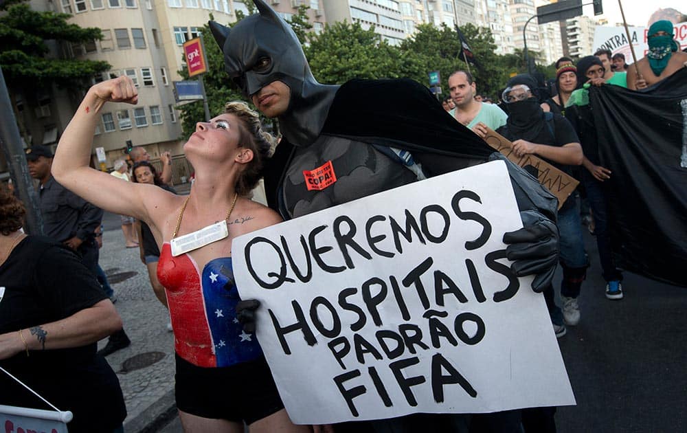 A man dressed as Batman holds a sign that reads in Portuguese `We want FIFA quality hospitals` as a woman in a super hero costume flexes her muscles at a protest demanding better public services in Rio de Janeiro, Brazil.