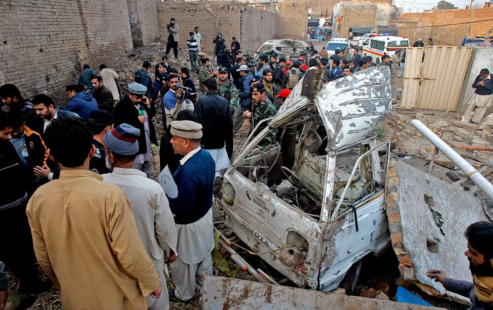 People gather at the site of an explosion in Peshawar, Pakistan. A bomb hauled into a car repair shop in northwestern Pakistan has killed several people and left many injured, police official said.