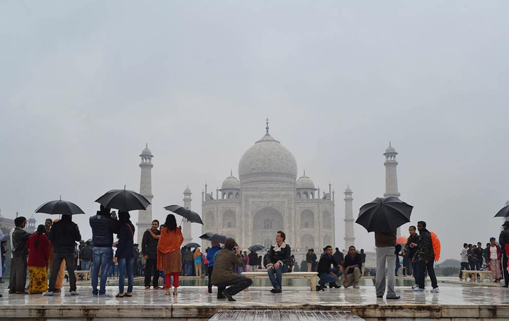 Tourists hold umbrellas to protect themselves from the rain in front of the Taj Mahal monument in Agra, India.