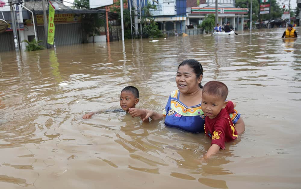 Indonesians women carrying her son wades through a flooded street with another son in Jakarta. Flooding caused by monsoon rains have forced thousands of people to flee their homes in Indonesia`s capital.