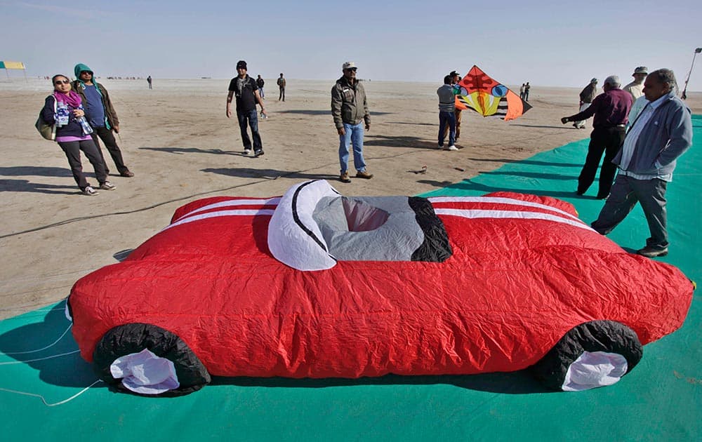 People stand near a car-shaped kite at the International Kite Festival at white sand in the Rann of Kutch, a seasonal salt marsh located in the Thar Desert, in Dhordo, about 500 kilometers from Ahmedabad.