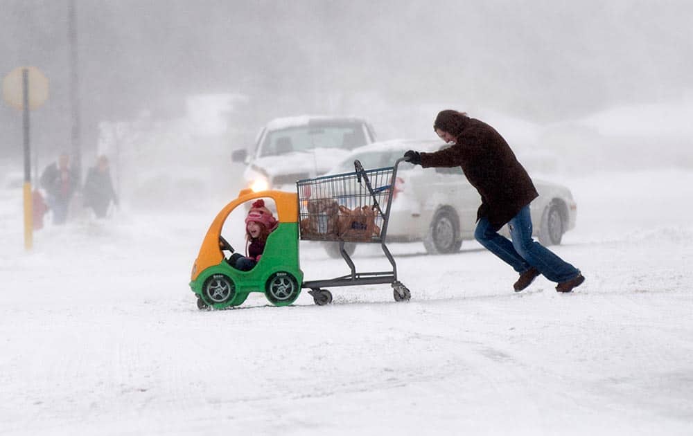 A woman pushes her daughter and their groceries through blowing snow in the Kroger parking lot in Green Acres Plaza on State Street in Saginaw Township, Mich.