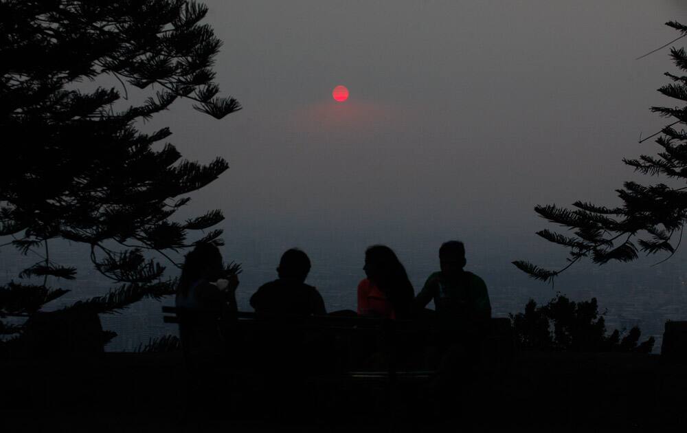 A group of people relax on a park bench at Cerro San Cristobal Park overlooking the Chilean capital which is shrouded by a cloud of smoke from dozens of forest fires that burn near Santiago, Chile.