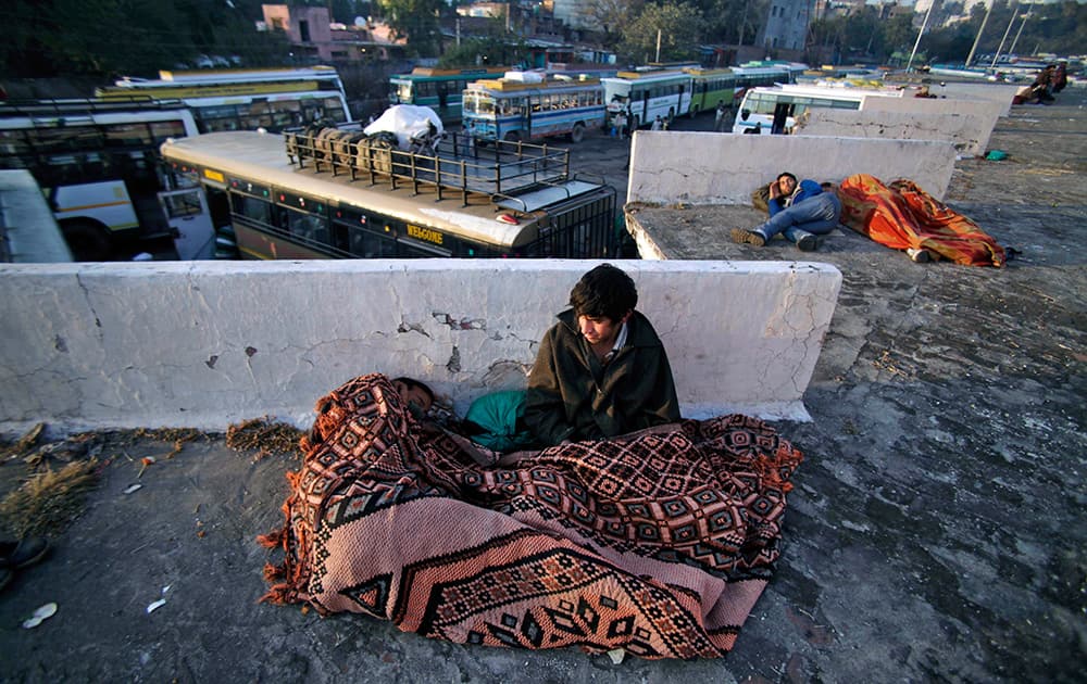 Stranded passengers rest wrapped in blankets as they wait for the Jammu-Srinagar highway to reopen at a bus station in Jammu.