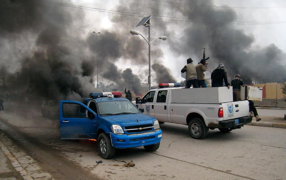Al-Qaida fighters patrol in a commandeered police truck passing burning police vehicles in front of the main provincial government building, in Fallujah, 40 miles (65 kilometers) west of Baghdad, Iraq.