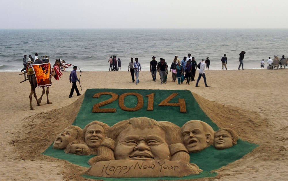 People walk near the sand sculpture to celebrate the new year 2014 created by sand artist Sudarshan Pattnaik at the Puri sea beach, 67 kilometers (42 miles) away from the eastern Indian city of Bhubaneswar, India.