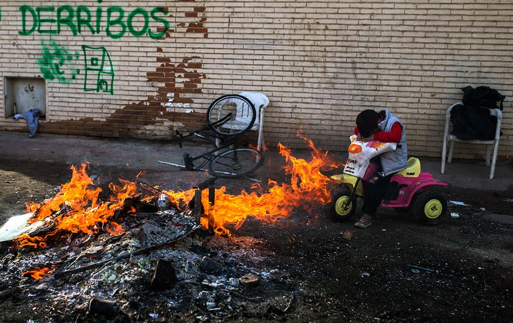 Antonia Navarro`s son Juan, 5, covers his face from the smoke of a fire lit by his family to keep themselves warm in the suburbs of Madrid, Spain.