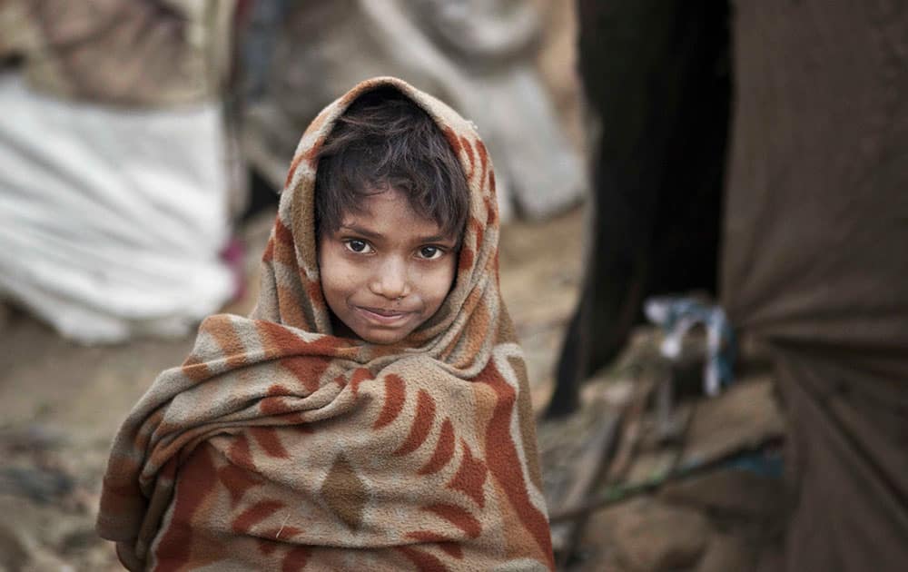 A young Indian boy wrapped in a shawl walks outside his makeshift tent on a cold day in New Delhi.