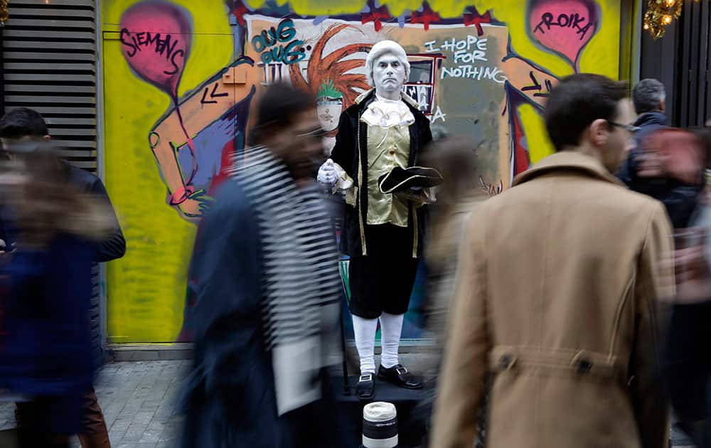 Athenians walk past a street performer dressed in 18th century style costume as anti-austerity slogans are seen on the wall behind, at Ermou main shopping street of Athens.