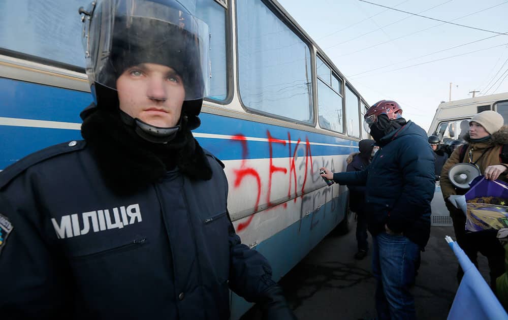 A riot police officer looks on as a pro-European Union activist writes an anti-presidential graffiti on a riot police bus a few hundred meters from Ukrainian President Viktor Yanukovych’s country residence of Mezhygirya outside Kiev, Ukraine.