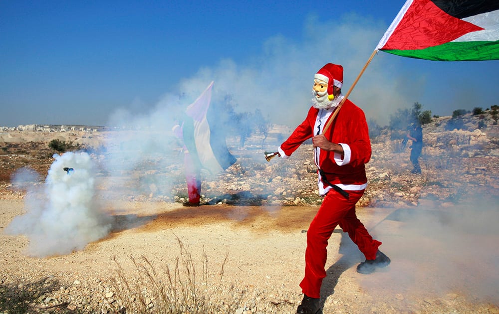 A Palestinian protester wearing a Santa Claus costume runs away from a tear gas canister fired by Israeli troops during a protest against Israel`s separation barrier outside the West Bank village of Bilin, near Ramallah.