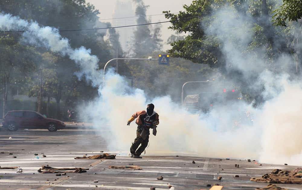 An anti-government protester runs away from tear gas canister fired by riot police near a gymnasium in Bangkok, Thailand.