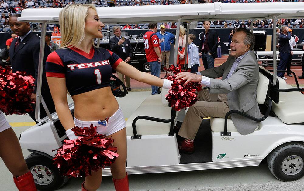 Former United States President George H. W. Bush, right, greets a Houston Texans cheerleader before an NFL football game against the New England Patriots.