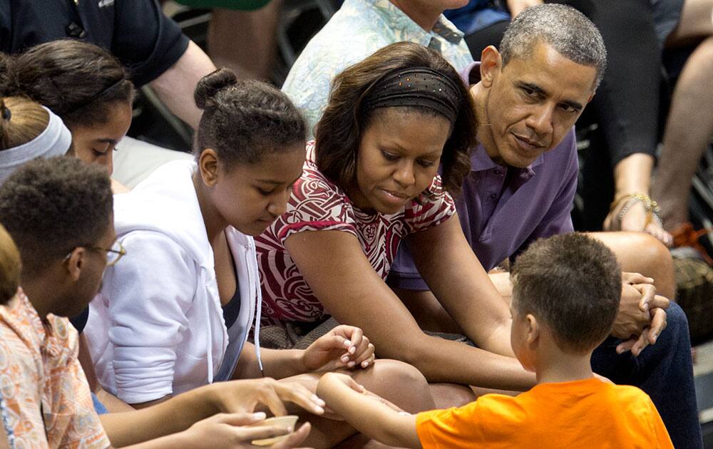 President Barack Obama and first lady Michelle Obama with daughter Sasha, third from right, and Malia, fourth from right sit with family members and friends during the Oregon State University versus University of Akron college basketball game at the Diamond Head Classic at the Stan Sheriff Center in Honolulu.