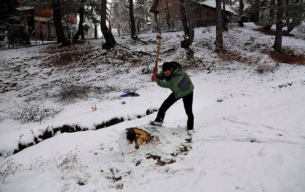 A Kashmiri man cuts a wooden log as he stands on a snow covered field on the outskirts of Srinagar, India.