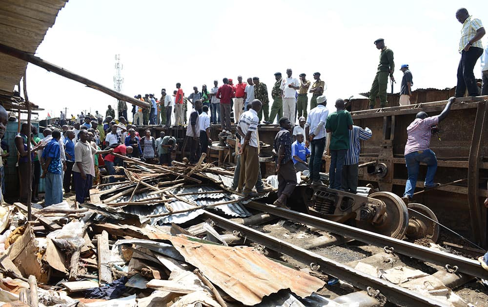 Kenyans gather around the remains of a house which lies on train tracks next to a train carriage on its side, after a cargo train derailed in Nairobi, Kenya.