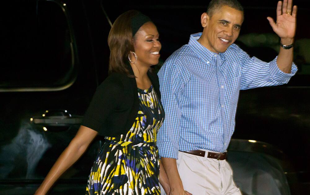 President Barack Obama, right, waves while escorting the first lady Michelle Obama, left, to meet various well wishers after disembarking Air Force One at Joint Base Pearl Harbor-Hickam in Honolulu.