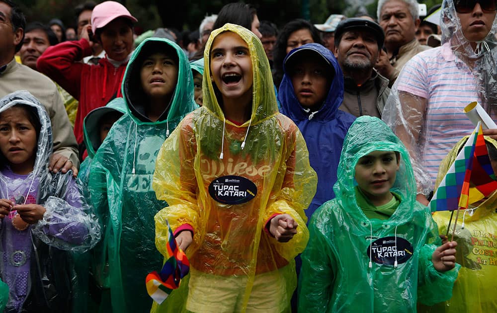 Children wearing raincoats watch the country’s first telecommunications satellite launch in China during a live broadcast in La Paz, Bolivia.