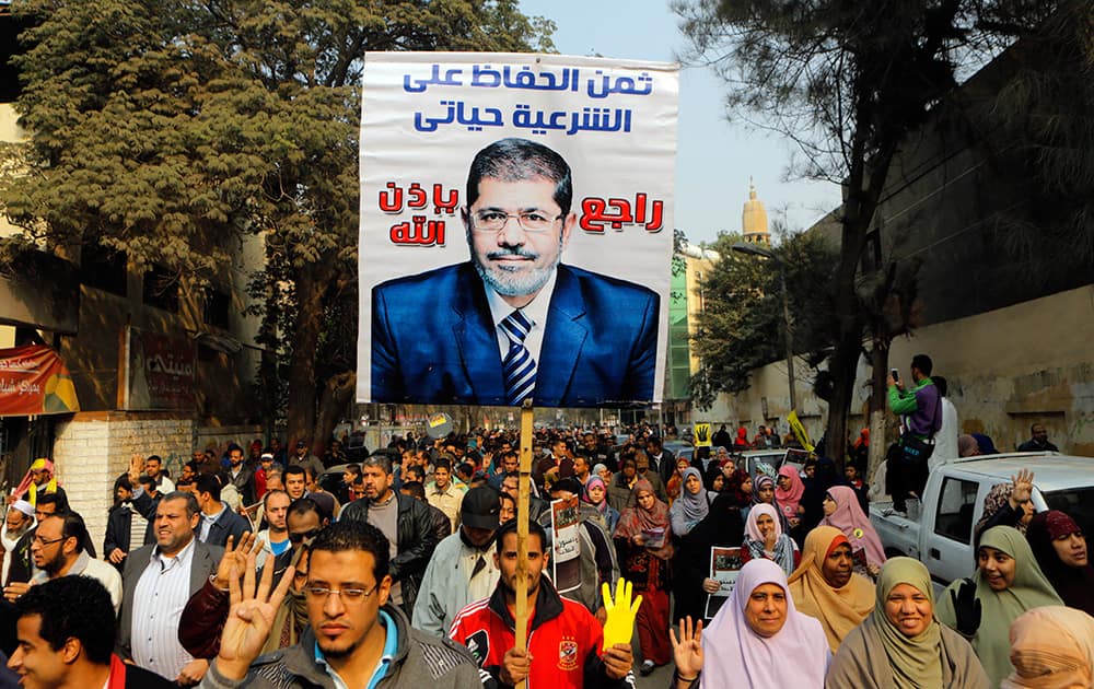 Supporters of Egypt`s ousted President Mohammed Morsi hold his poster as they raise their hands with four fingers which has become a symbol of the Rabaah al-Adawiya mosque, where Morsi supporters had held a sit-in for weeks that was violently dispersed in August, during a protest in Cairo, Egypt.