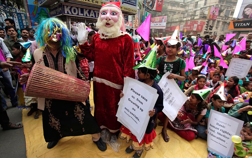 A folk singer performs and a man dressed as Santa Claus waves as underprivileged children wear festive hats and hold placards during a sit-in demonstration demanding basic human rights in Kolkata.