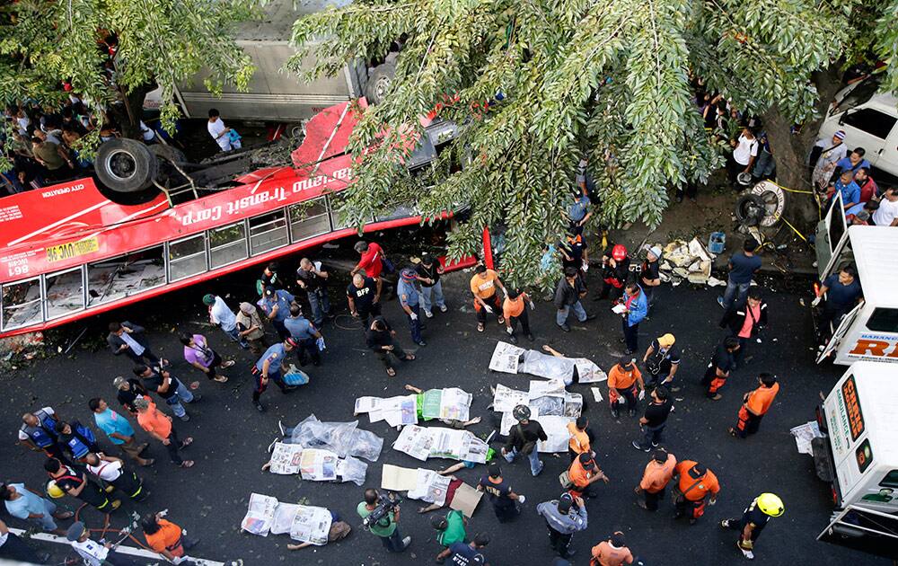 Bodies of passengers are covered in newspapers as they are laid down on the road after a passenger bus plunged from an elevated highway known as the Skyway Monday, Dec. 16, 2013, in suburban Paranaque southeast of Manila, Philippines. Officials said at least 21 people died, mostly passengers, and more than 20 others were injured in the accident.