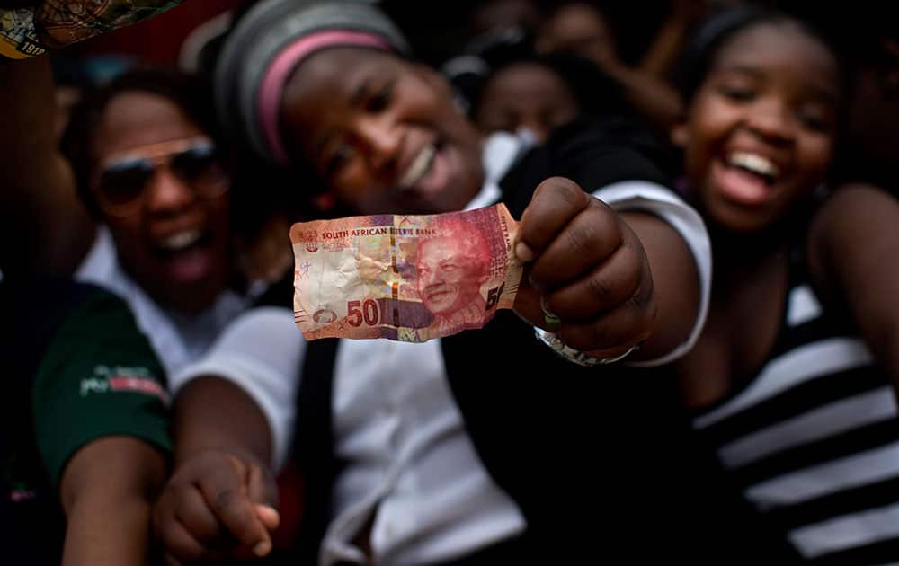 A woman shows a South African bill with the face of Late President Nelson Mandela while waiting Mandela`s convoy to pass by the town of Mthatha on its way to Qunu, South Africa.