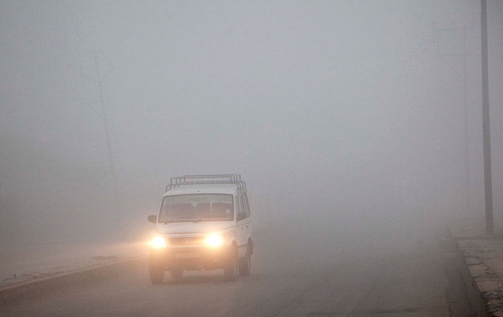 A vehicle moves with headlights on as dense fog envelopes on the outskirts of Srinagar, India.